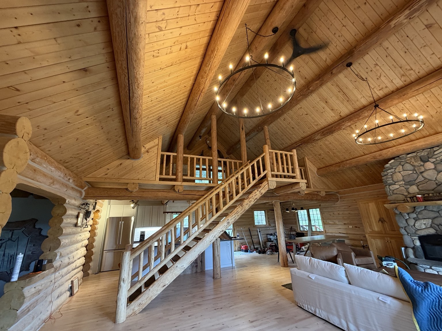 Log cabin interior with wood staircase, loft railings, and ring chandeliers