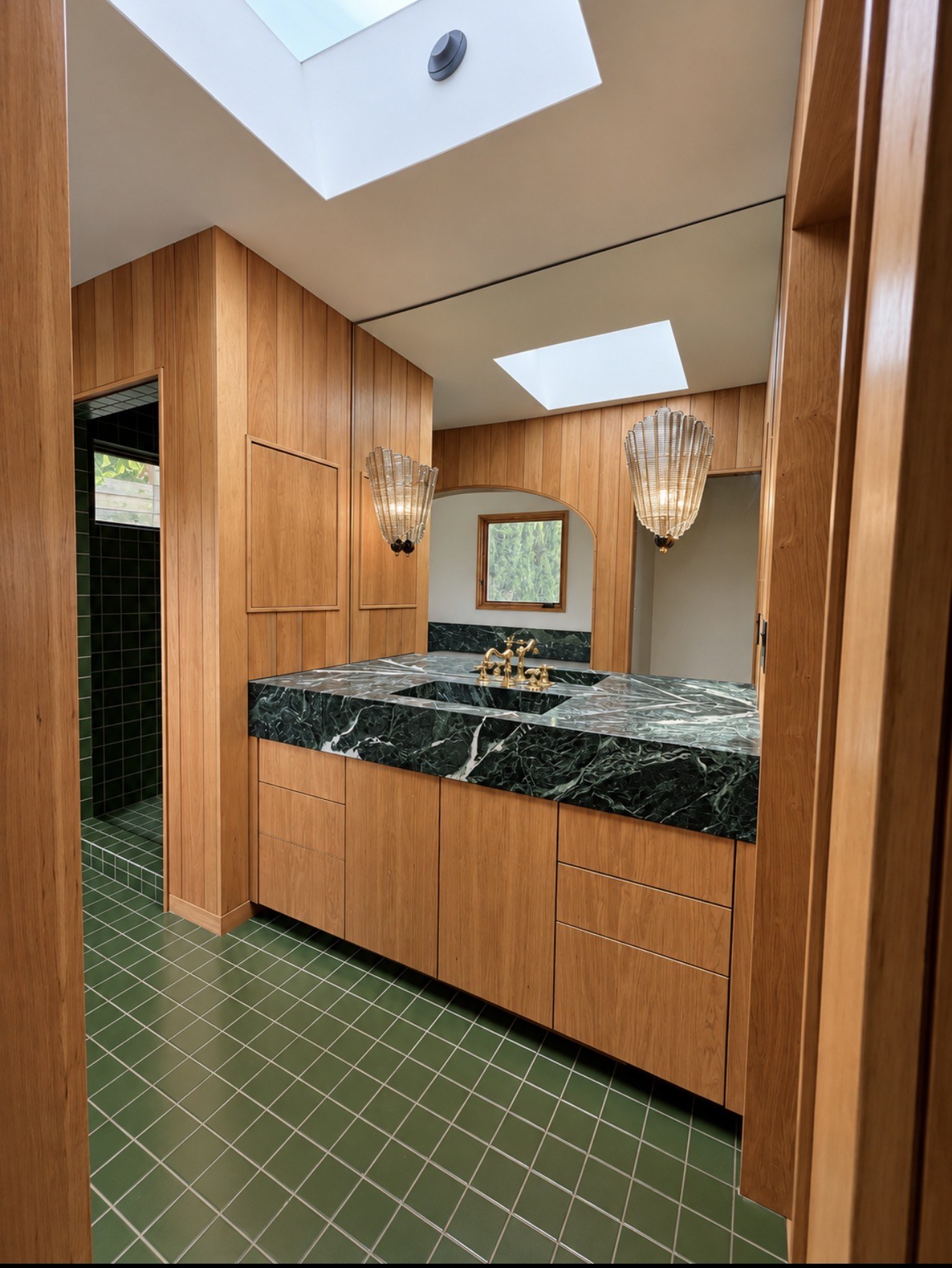 Wood vanity beneath a dark stone countertop with green tile floor